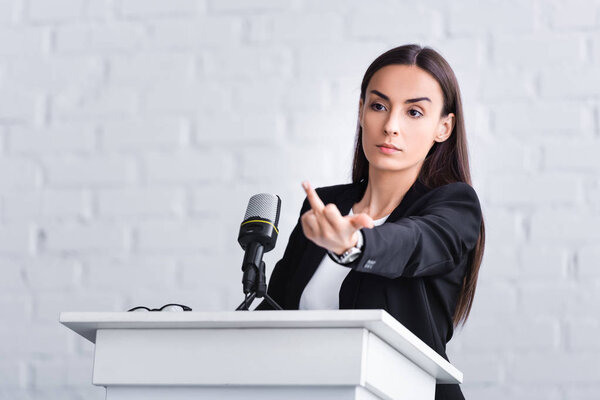 недовольный преподаватель, стоящий на трибуне в конференц-зале и показывающий средний палец
