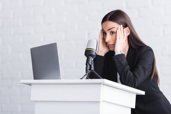 frightened lecturer standing on podium tribune and holding hands near head