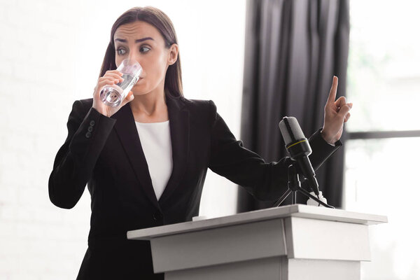 worried lecturer showing wait gesture while standing on podium tribune and drinking water