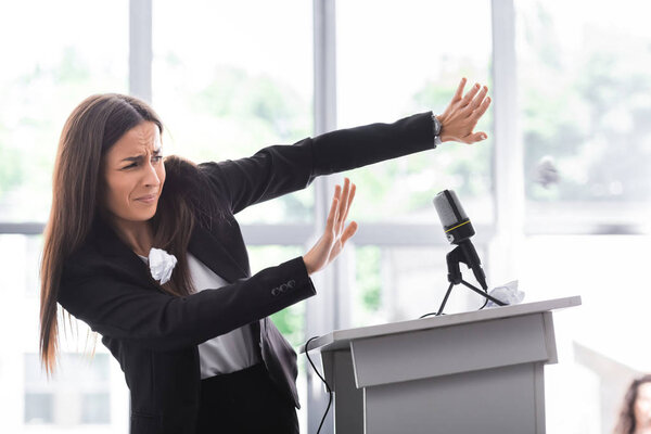 frightened lecturer, suffering from fear of public speaking, gesturing with hands while standing on podium tribune