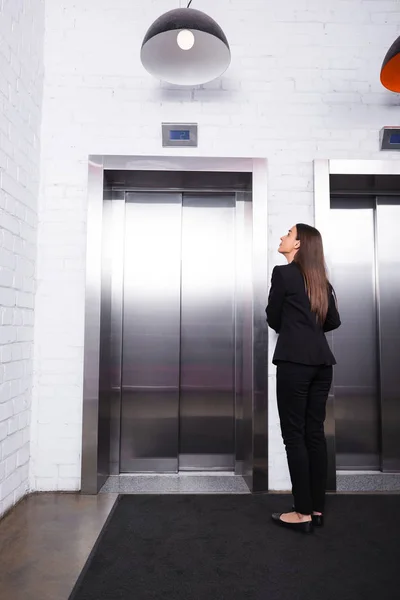 穿着正式服装的女商人站在大厅里等待电梯的后视图 — 图库照片
