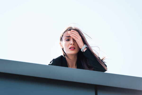 frightened businesswoman, suffering from acrophobia, looking down rooftop and covering face with hand