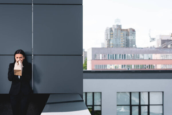 молодая бизнесвумен, страдающая от панической атаки, стоящая на крыше и дышащая в бумажный пакет
