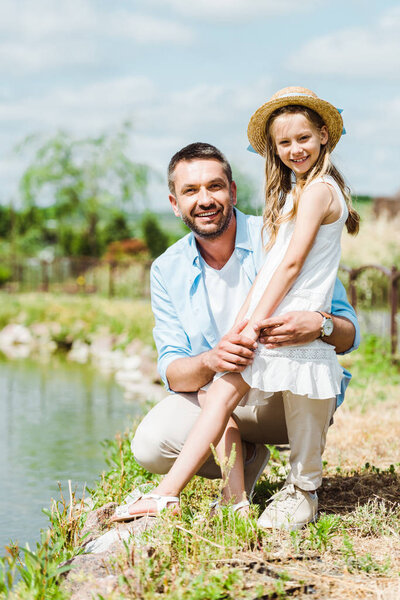 selective focus of cute kid standing near happy father and lake 