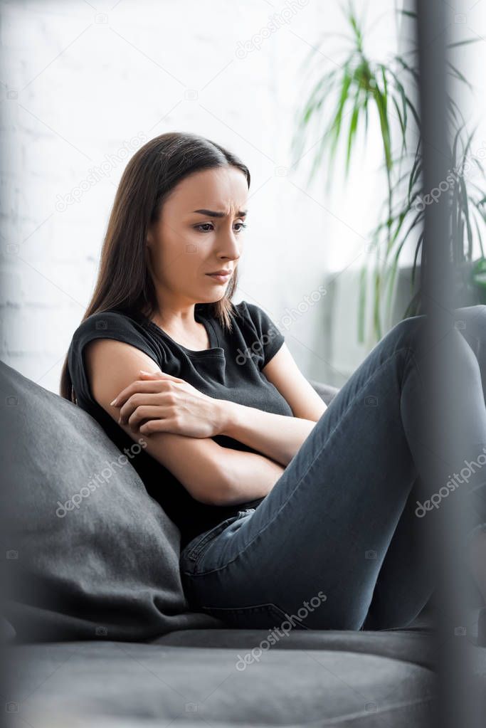 selective focus of crying young woman sitting on couch and suffering from depression