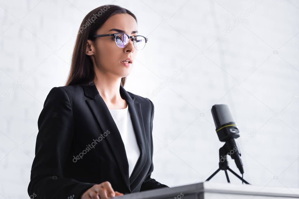 serious young lecturer in glasses and formal wear standing on podium tribune