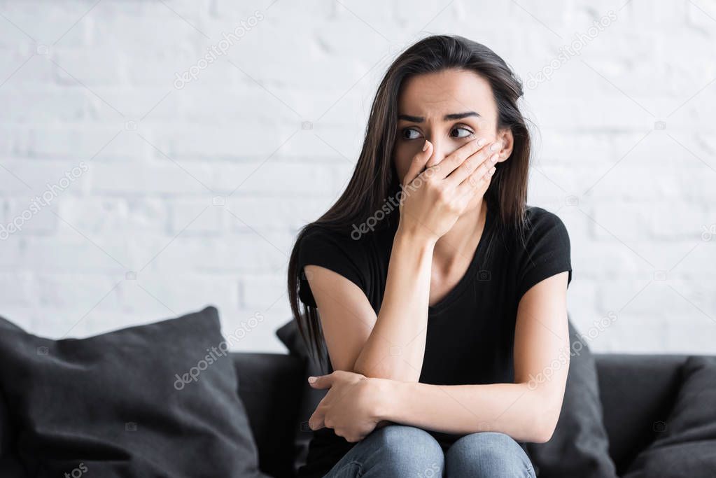 scared young woman holding hand on face and looking away while suffering from panic attack at home