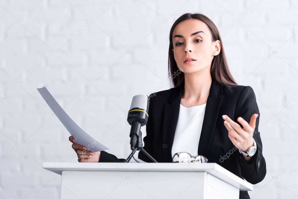 confident lecturer gesturing while speaking into microphone on podium tribune