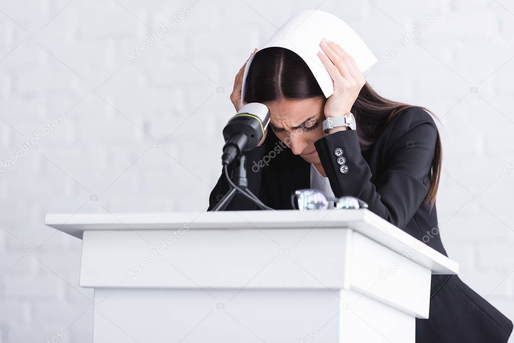 young lecturer, suffering from fear of public speaking, standing on podium tribune and covering head with paper