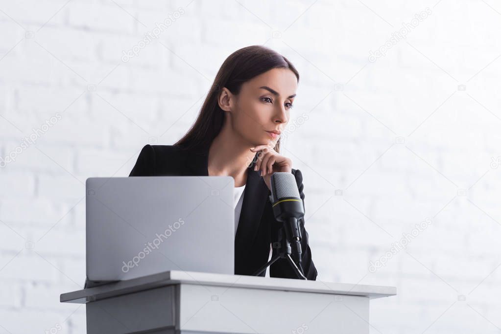 pensive lecturer standing on podium tribune near microphone and laptop