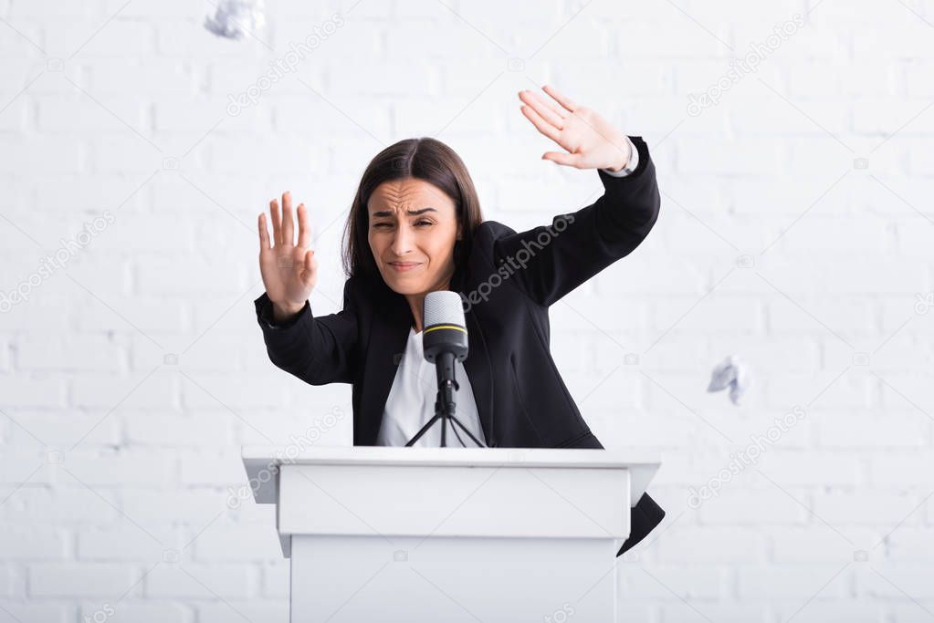frightened lecturer suffering from glossophobia gesturing with hands while standing on podium tribune