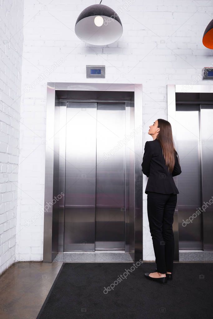 back view of businesswoman in formal wear standing in lobby and waiting for elevator