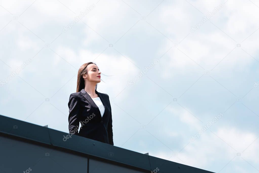 attractive, confident businesswoman smiling and looking away while standing on rooftop
