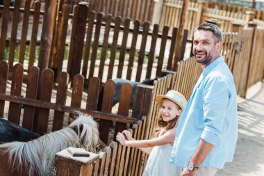 cheerful child and man smiling while standing near pony in zoo  clipart