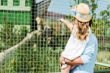 cropped view of father holding in arms daughter pointing with finger at cage with monkey  clipart