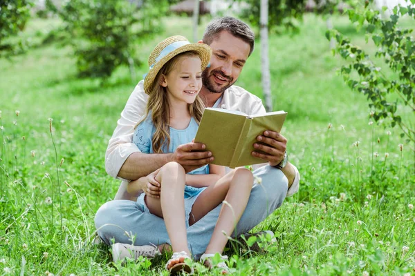 Vrolijke Vader Dochter Zittend Gras Lezen Boek — Stockfoto