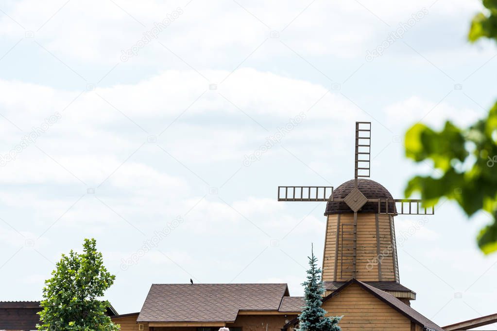 selective focus of windmill near houses and green trees 