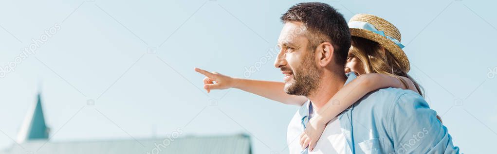 panoramic shot of cheerful man piggybacking daughter pointing with finger