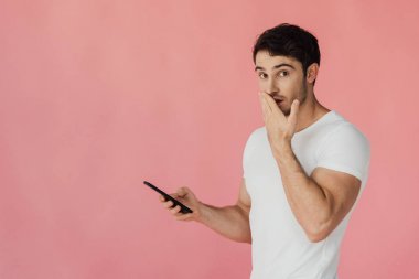 akıllı telefon kullanarak beyaz t-shirt şaşırttı kaslı adam ve el ile ağız kapsayan pembe izole