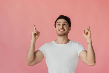 parmakları ile işaret ve pembe izole bakarak beyaz t-shirt heyecanlı kaslı adam ön görünümü