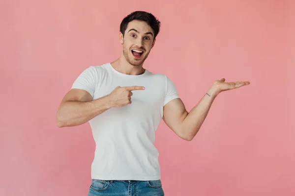 兴奋的肌肉男子在白色T恤指着手和指点与粉红色隔离的手指 — 图库照片
