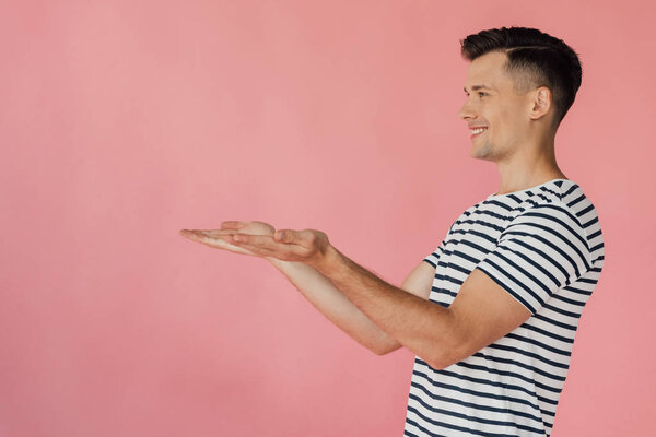 smiling man in striped t-shirt pointing with hands isolated on pink