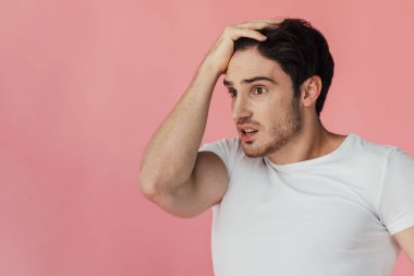 shocked muscular man in white t-shirt touching head isolated on pink clipart