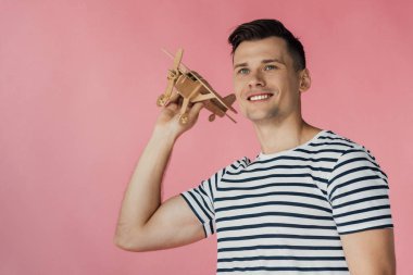 pembe izole ahşap oyuncak uçak tutan çizgili t-shirt gülümseyen genç adam