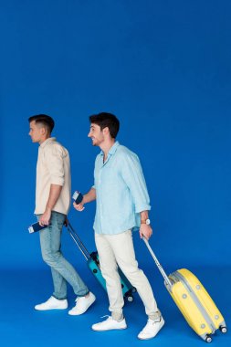 mavi üzerinde uçak bileti ile bavul ve pasaport tutan iki turist tam uzunlukta görünümü