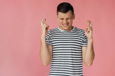 pembe izole çapraz parmakları ile çizgili t-shirt endişeli genç adamın ön görünümü