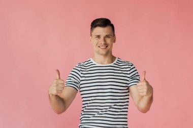 pembe izole başparmak gösteren çizgili t-shirt gülümseyen genç adamın ön görünümü