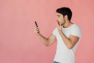 beyaz t-shirt pembe izole akıllı telefon tutan korkmuş kaslı adam