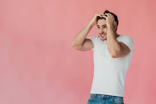шокированный мускулистый мужчина в белой футболке касаясь головы, изолированной на розовый
