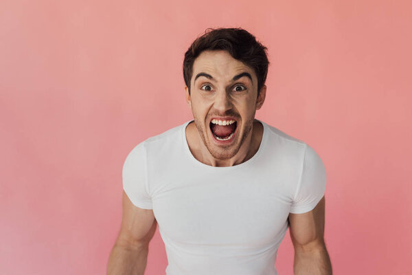 вид разгневанного мужчины, кричащего и смотрящего на камеру, изолированную от розового

