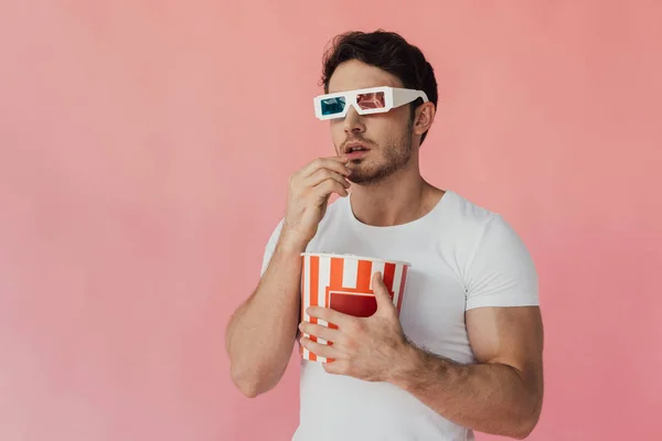 好奇的肌肉男子在3D眼镜吃爆米花隔离在粉红色 — 图库照片