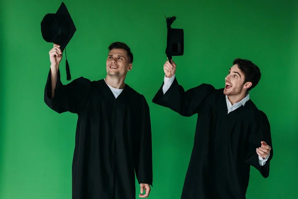 Dwóch Podekscytowany Studentów Posiadających Czapki Akademickie Izolowane Zielono — Zdjęcie stockowe