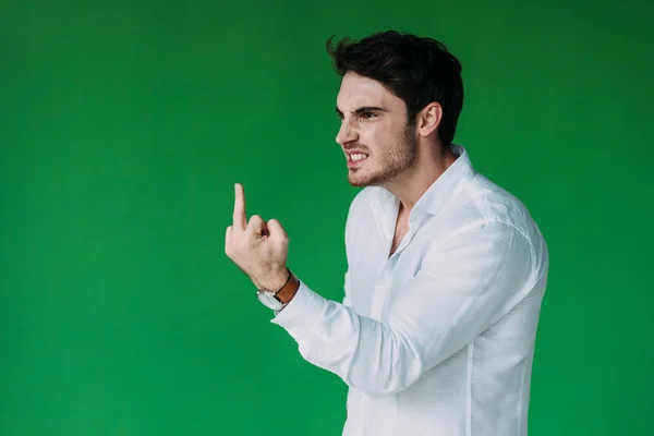 stock image angry man in white shirt looking away and showing middle finger isolated on green
