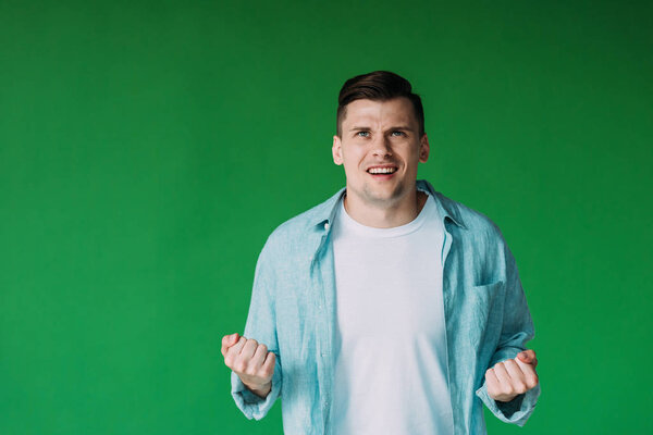 front view of irritated young man in shirt holding fists up isolated on green