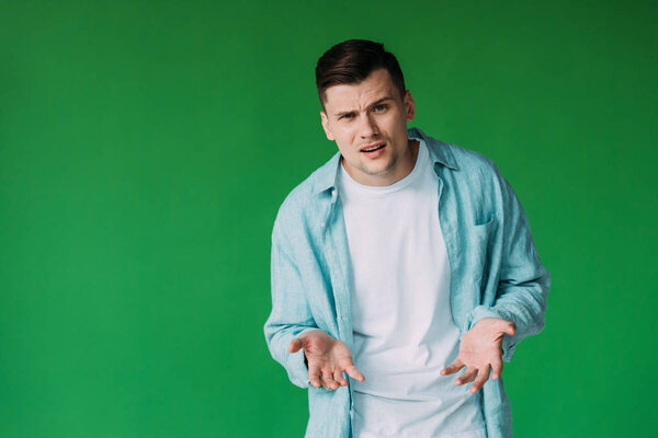 irritated young man in shirt gesturing isolated on green