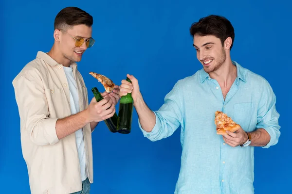 Dois Amigos Sorridentes Segurando Garrafas Cerveja Fatias Pizza Isoladas Azul — Fotografia de Stock