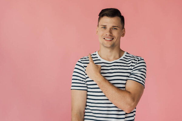 front view of smiling young man in striped t-shirt looking at camera isolated on pink