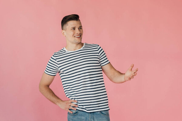 smiling young man in striped t-shirt with hand on hip isolated on pink