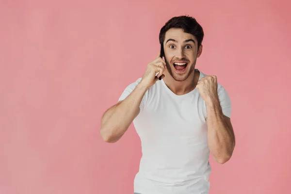 白いTシャツを着た興奮した筋肉の男がスマートフォンで話し ピンクで孤立したイエスジェスチャーを見せる正面図 — ストック写真