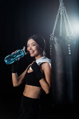 mutlu kız spor şişe tutan ve siyah izole kum torbası yakınında duran 