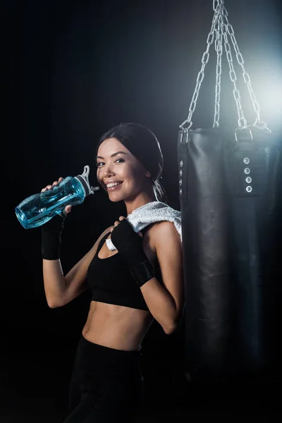 Chica Feliz Sosteniendo Botella Deporte Pie Cerca Saco Boxeo Aislado — Foto de Stock