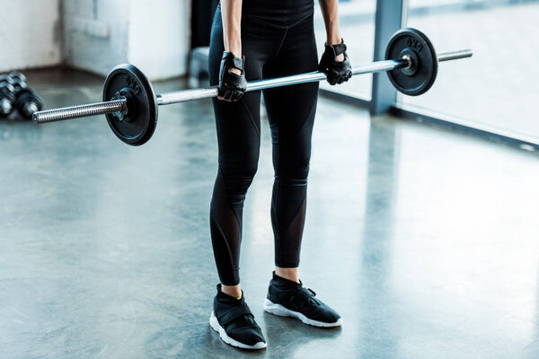 cropped view of young woman in sportswear working out with barbell in gym 