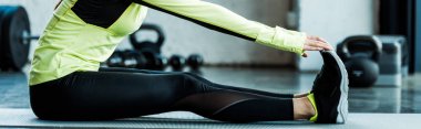 panoramic shot of young woman stretching on fitness mat in gym 