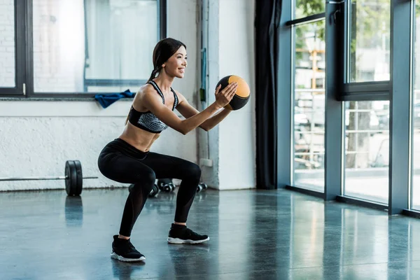 Cheerful Sportswoman Holding Ball Doing Squat Exercise — Stock Photo, Image