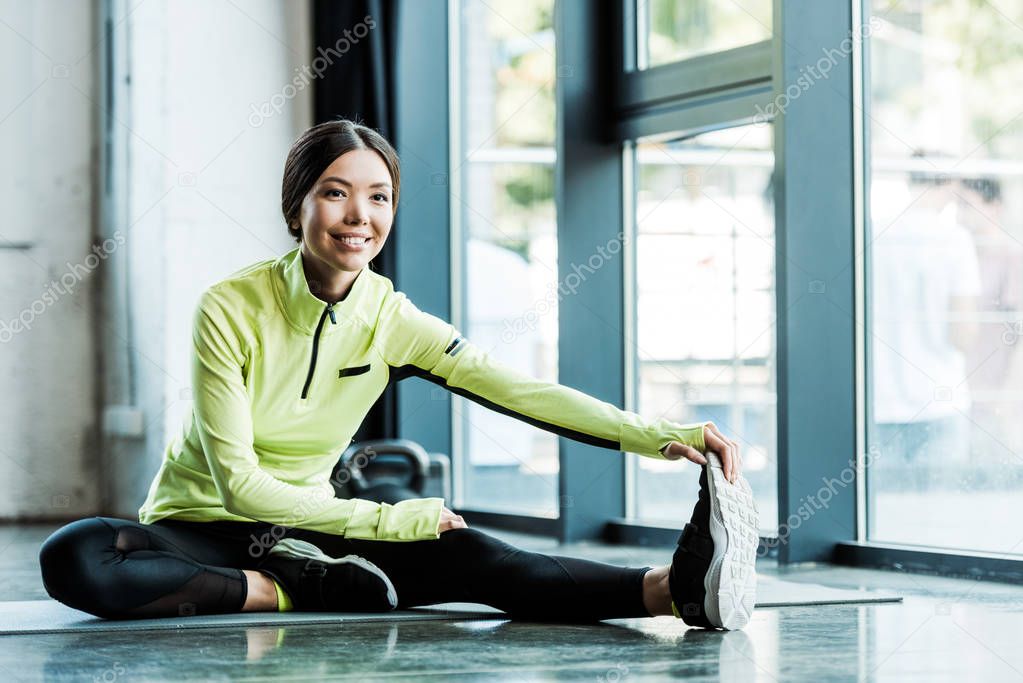cheerful young woman stretching on fitness mat in gym 