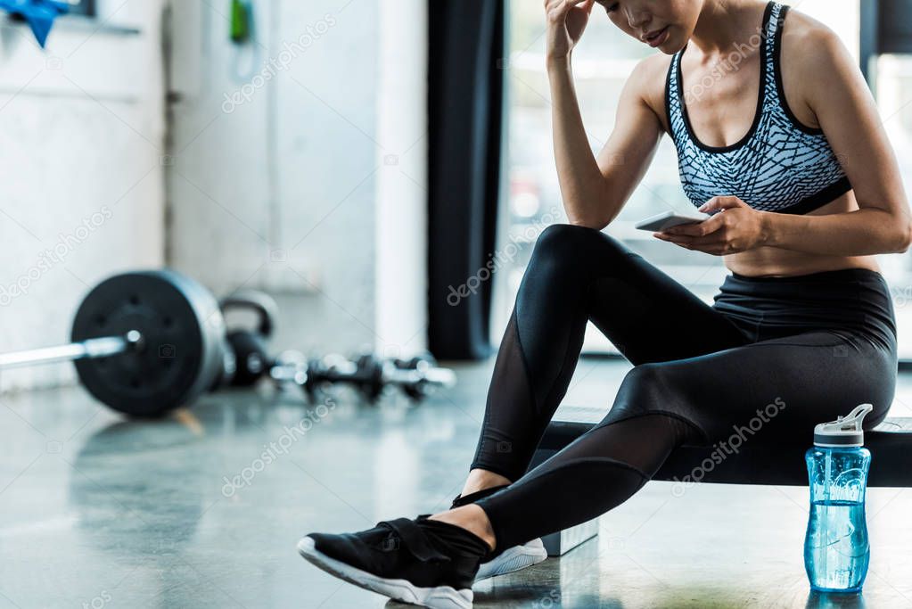 cropped view of sportswoman sitting on step platform and using smartphone 